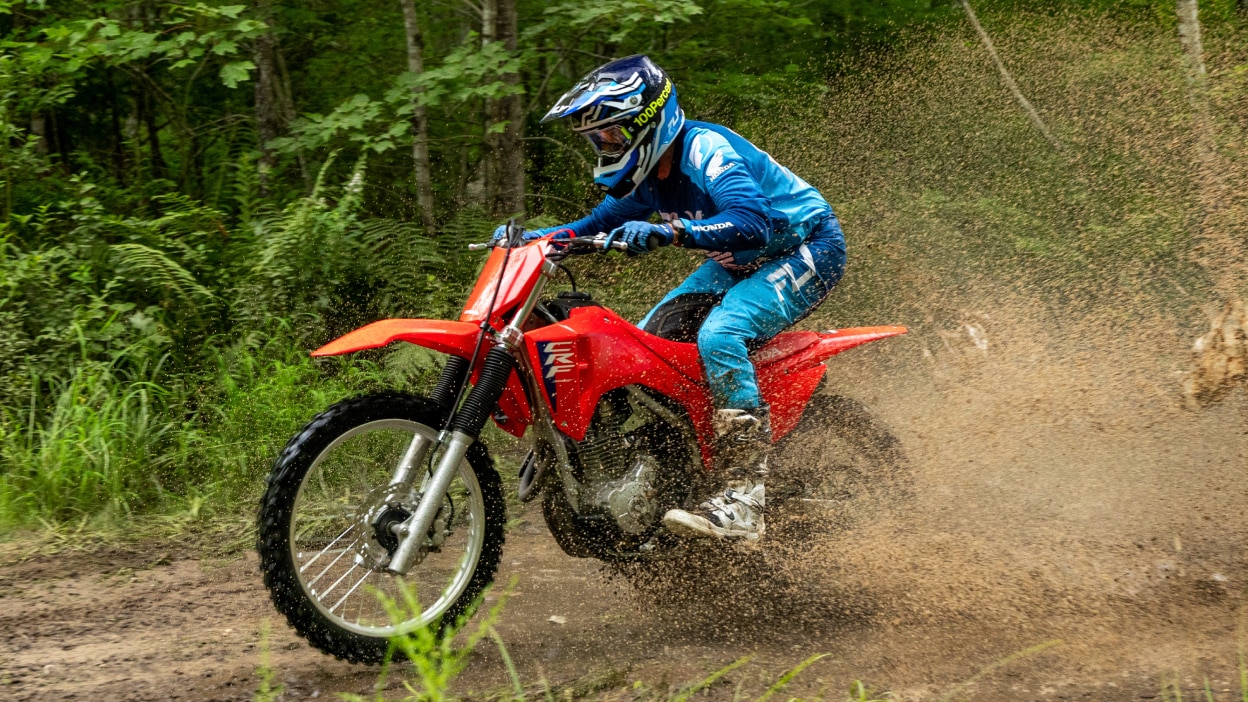 Pilote sur CRF300F allant à gauche. Paysage forestier en arrière-plan.