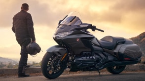 Right image of Gold Wing Tour stationary on road. Rider with helmet in hand standing to the right of Gold Wing Tour.
