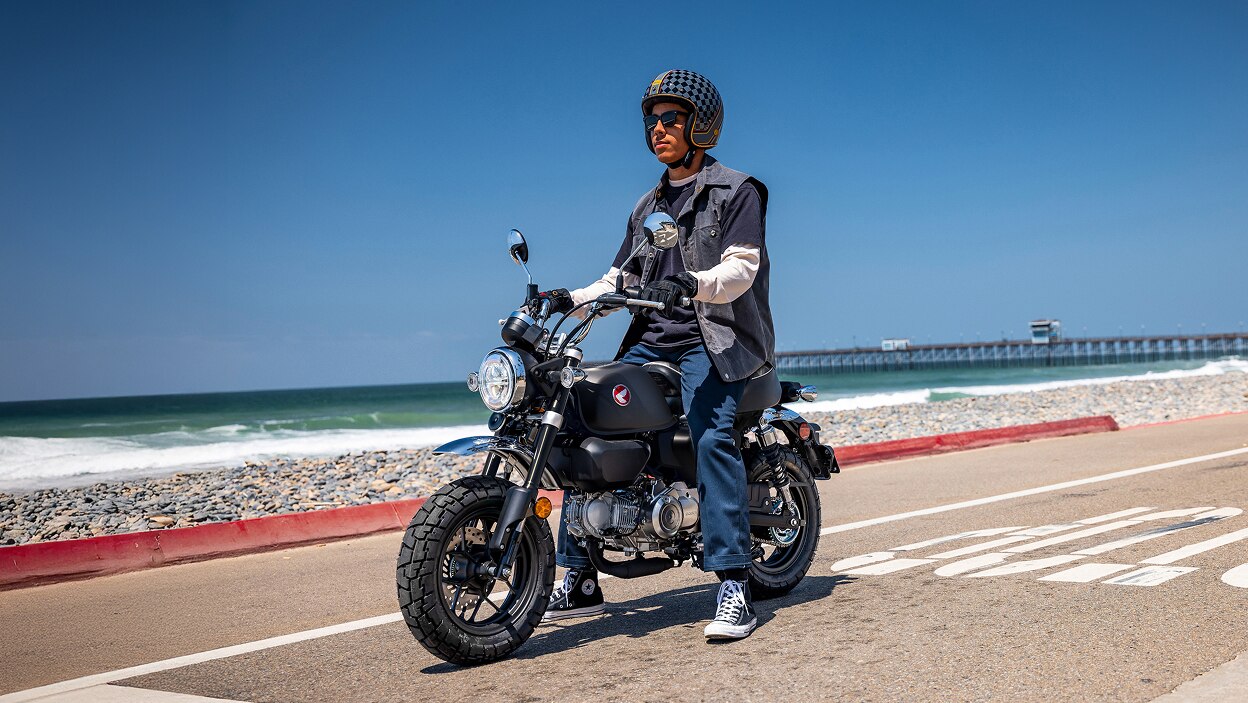 Motard à moto. À l'arrêt sur la route, face à gauche. Plage en arrière-plan.