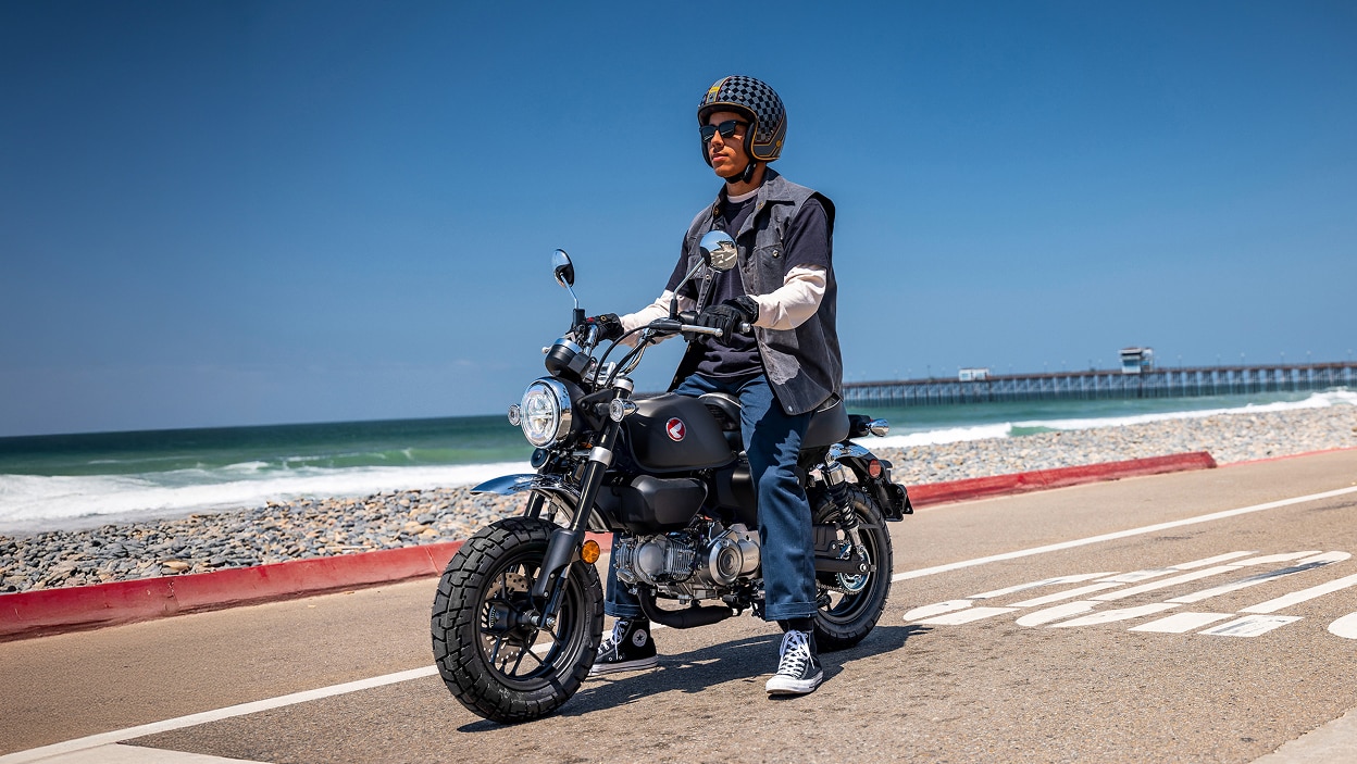 Motard à moto. À l'arrêt sur la route, face à gauche. Plage en arrière-plan.