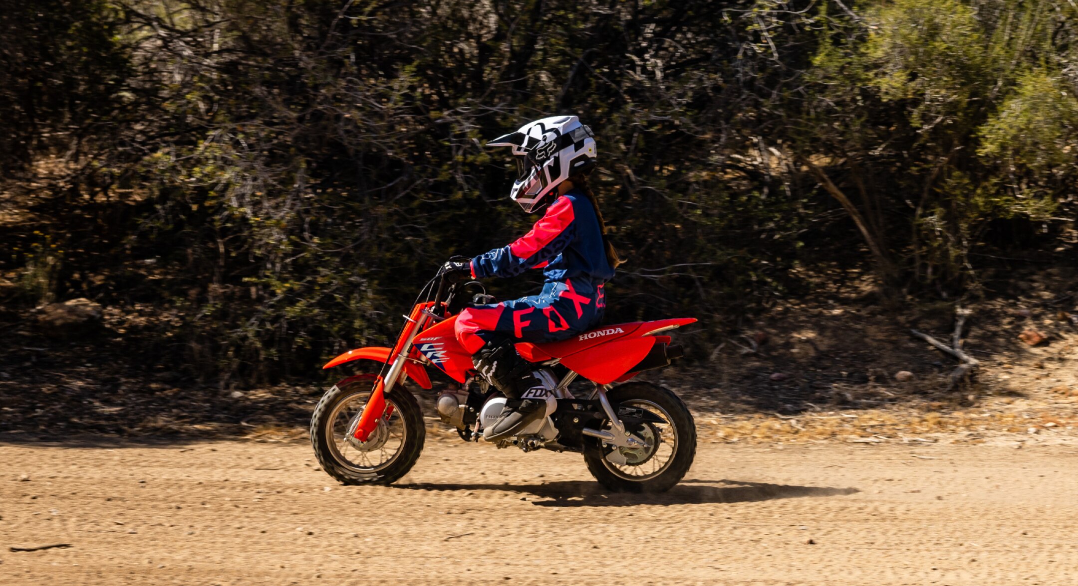 Young rider on bike going left on dirt road.