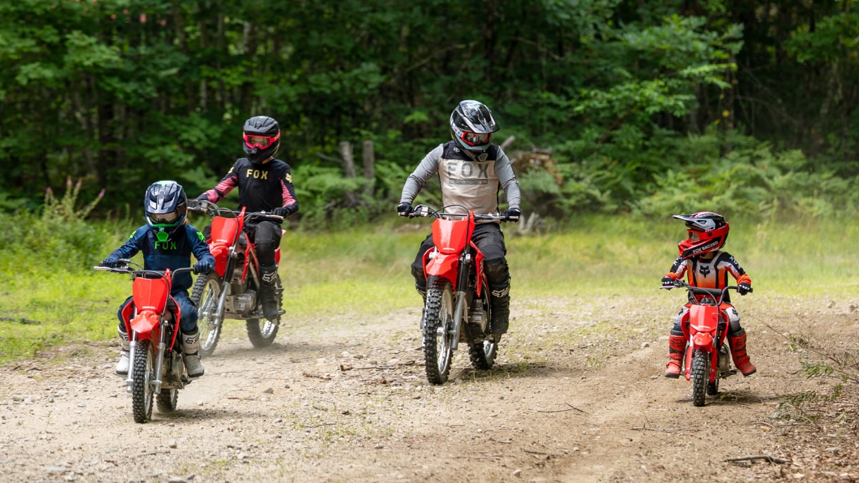A young rider practicing on a small red bike in a grassy field.