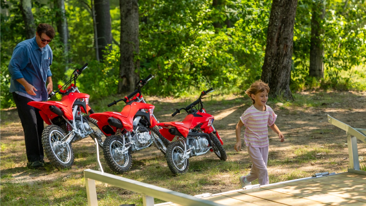 A father and child standing next to their motorcycles in a forest setting.