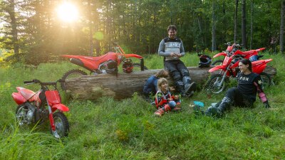 A wide shot of several riders parked on a grassy clearing in a wooded area, highlighting a family-friendly outdoor setting.