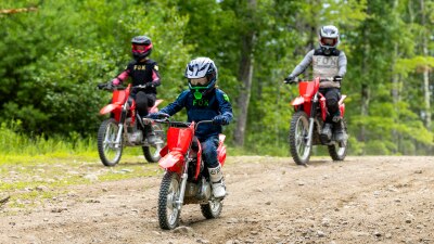 Three riders of different heights riding in a line on a narrow dirt trail, demonstrating a variety of bike sizes.