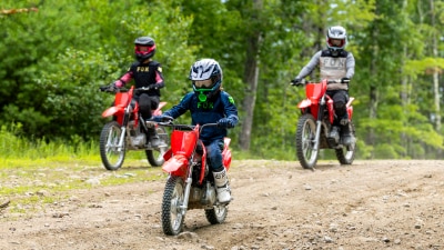 Three riders of different heights riding in a line on a narrow dirt trail, demonstrating a variety of bike sizes.
