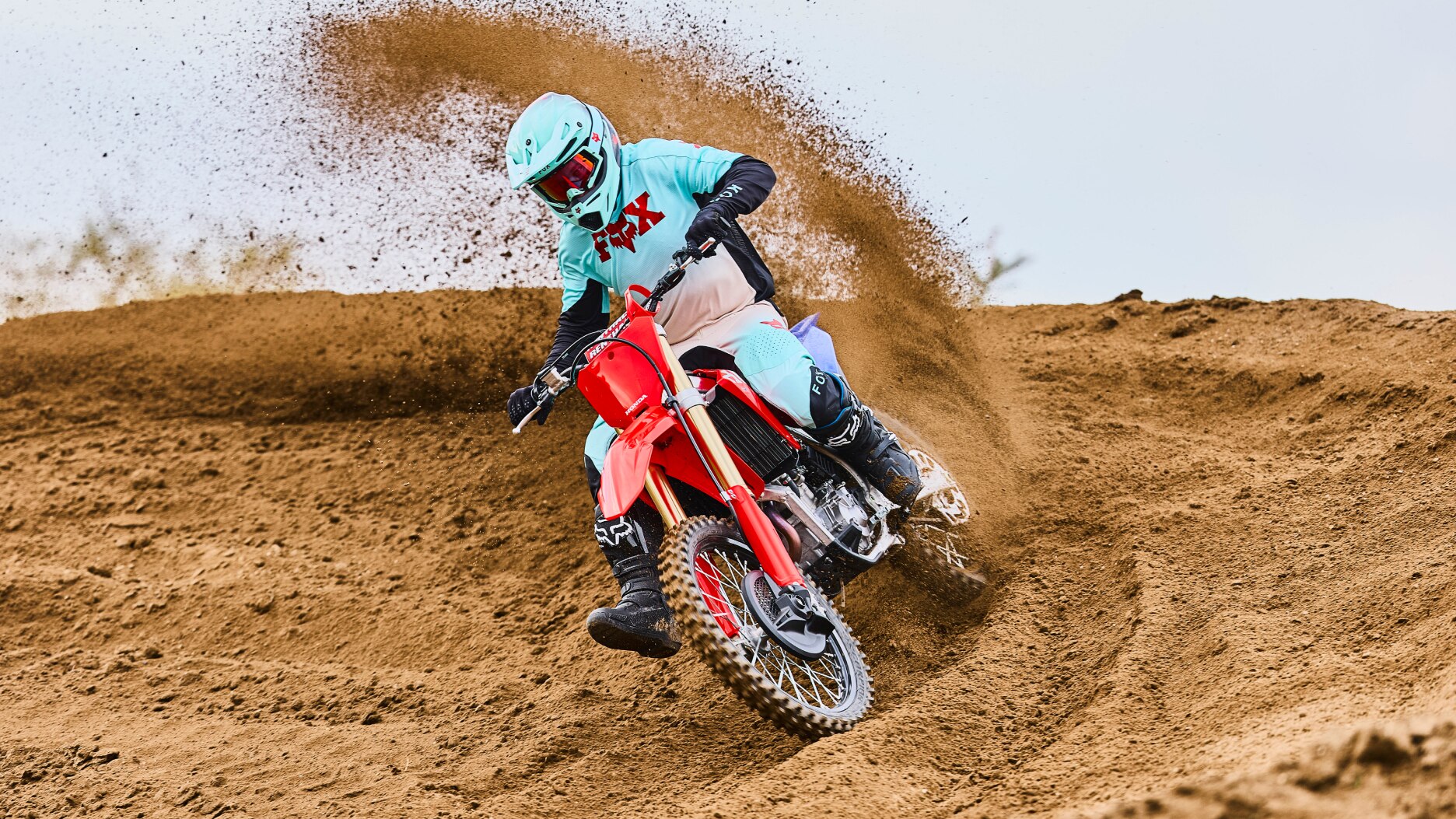 Motocross rider in teal gear turning sharply and kicking up dirt.