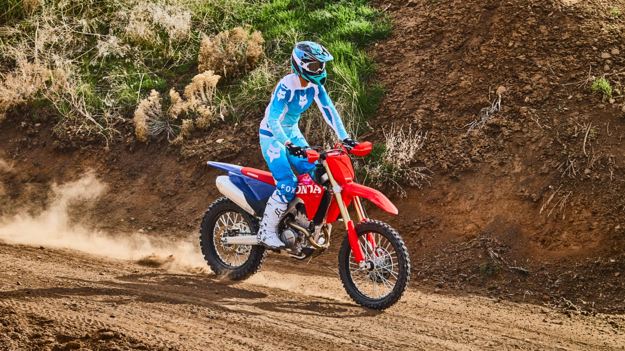 Motocross rider in teal gear riding a red dirt bike on a track.