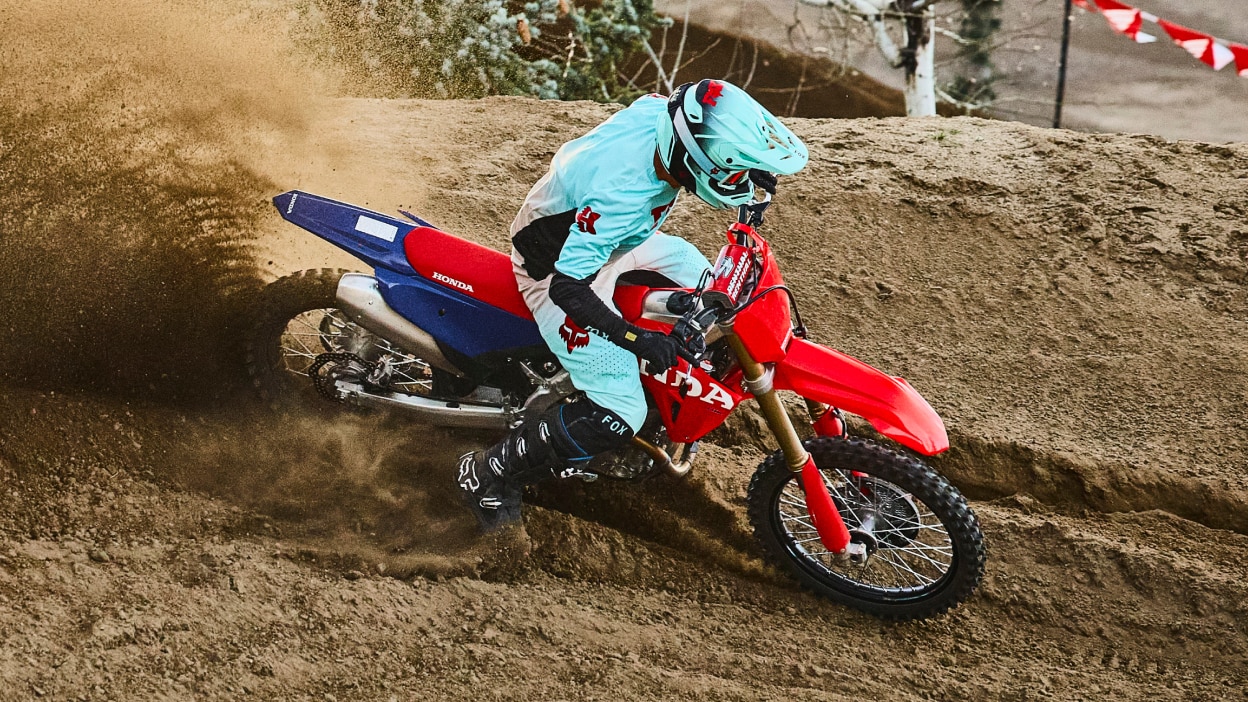 Motocross rider jumping a red dirt bike over a dirt crest.