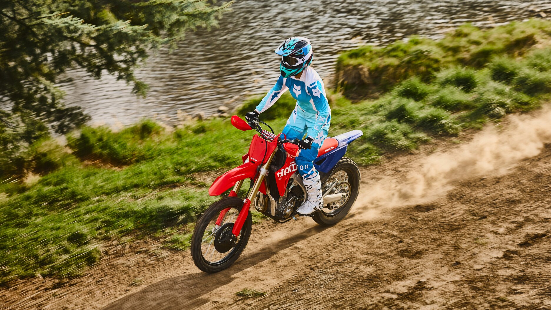 Motocross rider in teal gear racing on a dirt track.