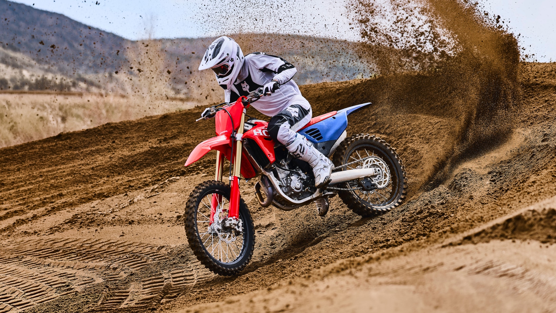 Motocross rider mid-air jumping over a dirt hill.