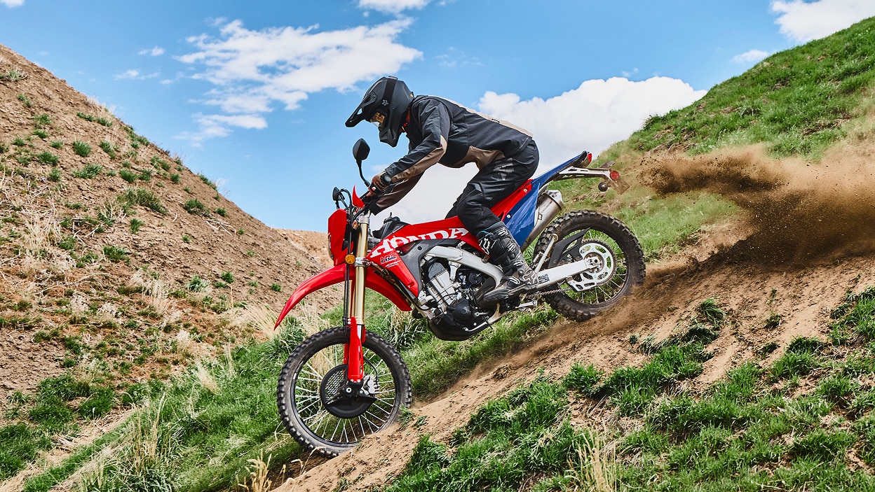 Un motard sur une moto double usage sur une colline herbeuse.