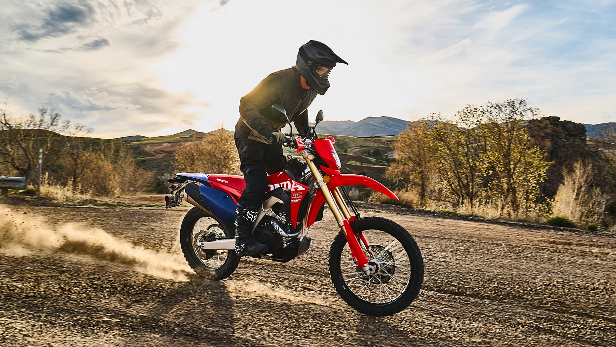 Un motard sur une moto double usage sur un sentier de terre.