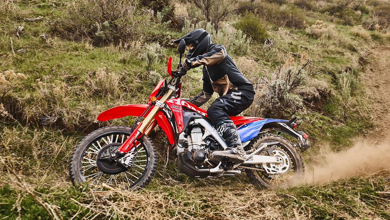 Un motard sur une moto double usage soulevant de la terre sur un sentier.
