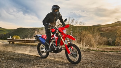 A motorcyclist riding a red dual sport motorcycle on a dirt road.