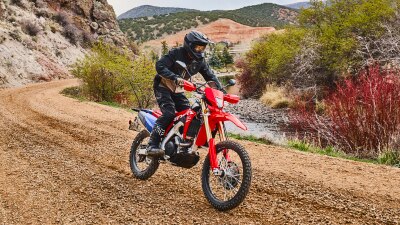 A rider maneuvering a red dual sport motorcycle on a tight dirt trail.