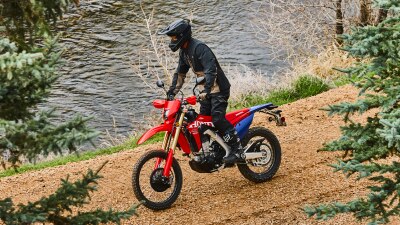 A motorcyclist riding a red dual sport motorcycle on an unpaved road.