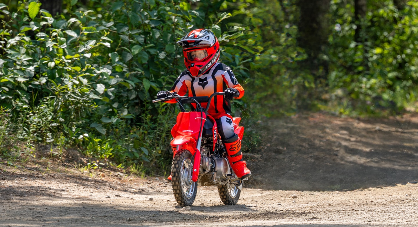 Gros plan d'un jeune pilote souriant tout en pilotant la CRF50F à travers un feuillage vert luxuriant.