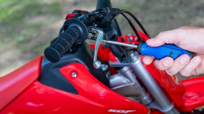 Close-up of a hand adjusting the throttle limiter screw on the handlebar.