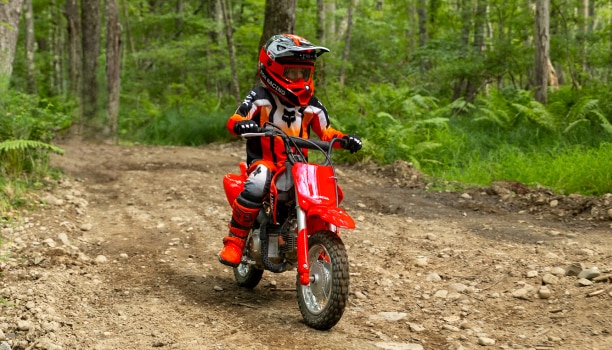 Front view of a young rider on a CRF50F approaching on a dirt trail.