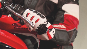 Close up view of a motorcycle glove gripping a  handlebar. / Gros plan d’un gant de motocycliste agrippant un guidon.