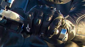 Close up of a hand in a black leather glove gripping the controls of a motorcycle.  / Gros plan d'une main dans un gant de cuir noir saisissant les commandes d'une moto.