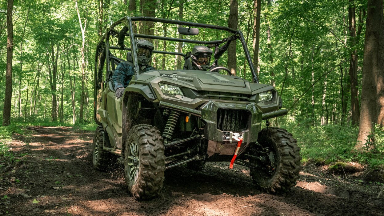 Two people with helmets in sxs going right. Green forrest background.