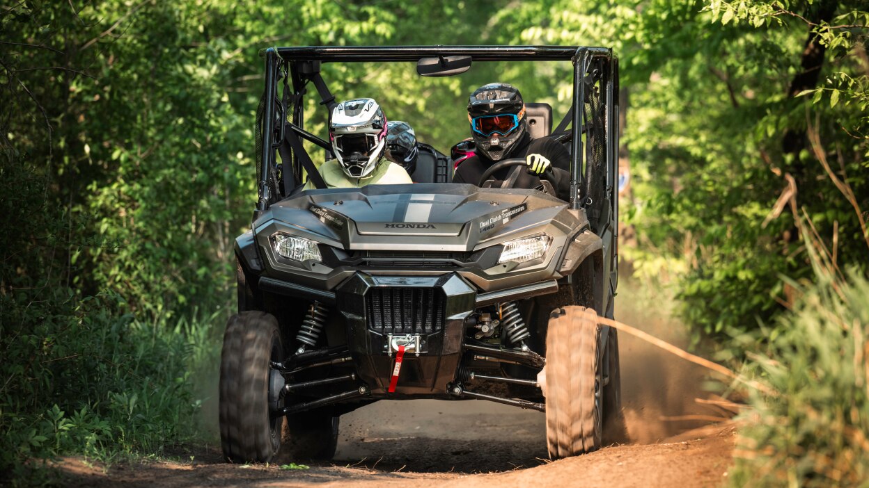 Four people in sxs going left in green forrest.