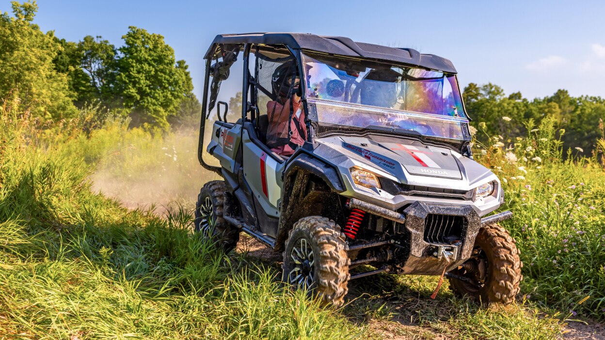 Pionnier à droite face à un chemin de terre. Arbres verts et buissons en arrière-plan. Poussière des pneus arrière.