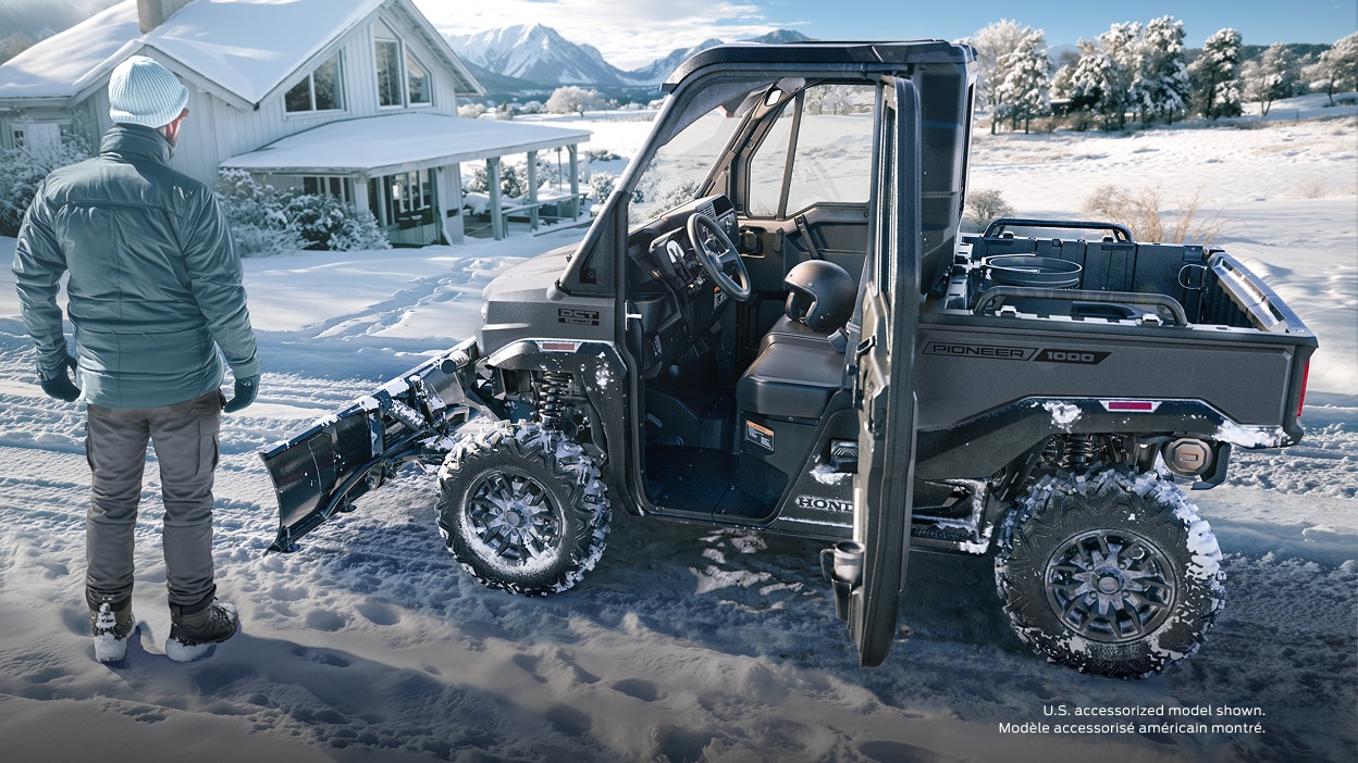 A Honda Pioneer 1000 driving through a snowy winter landscape.