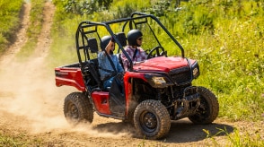A Honda Pioneer 520 driving on a dirt trail, kicking up dust.