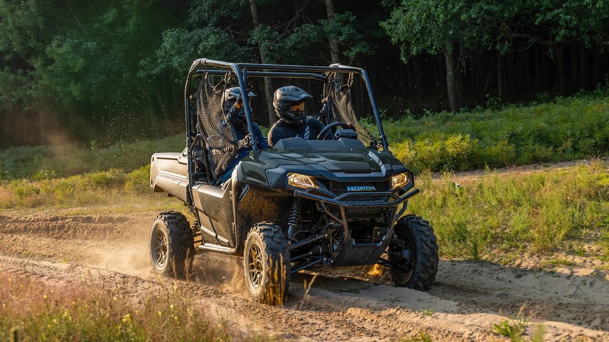 Petite image d'un Honda Pioneer 700 vert roulant sur un sentier de terre en forêt.