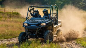 A blue Honda Pioneer 700 driving on a dusty dirt path.