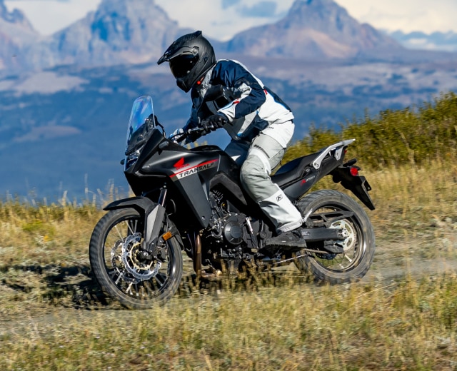 un pilote sur une moto Honda Transalp avec des montagnes en arrière-plan